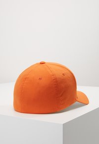 Cappellino da baseball in cotone arancione con visiera curva, dettagli cuciti e fori di ventilazione sul retro. Presenta una texture liscia e una forma arrotondata.