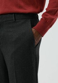 Grijze, op maat gemaakte broek met een gladde textuur, voorzien van een voorzak en een smalle pasvorm, gecombineerd met een rood geribde trui manchette.