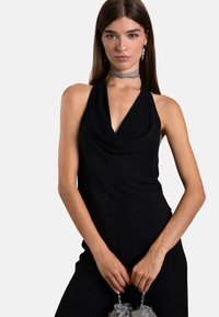 Schwarzes Haltertop mit drapiertem Stoff und tiefem Ausschnitt. Kombiniert mit einer silbernen Choker-Halskette und einer grauen, gerafften Handtasche. Glatte Textur.