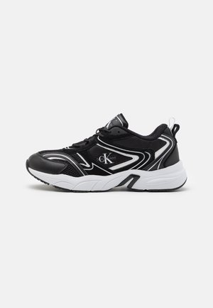 Czarno-białe sneakersy Calvin Klein z siateczkowymi i skórzanymi detalami, zawiązywane na sznurówki, z grubą białą podeszwą na jednolitym tle.