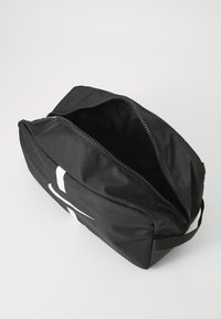 Schwarze Toilettentasche aus Stoff mit einem Reißverschluss oben, ausgestattet mit einem seitlichen Griff und einem auffälligen weißen Logo-Detail auf der Vorderseite.