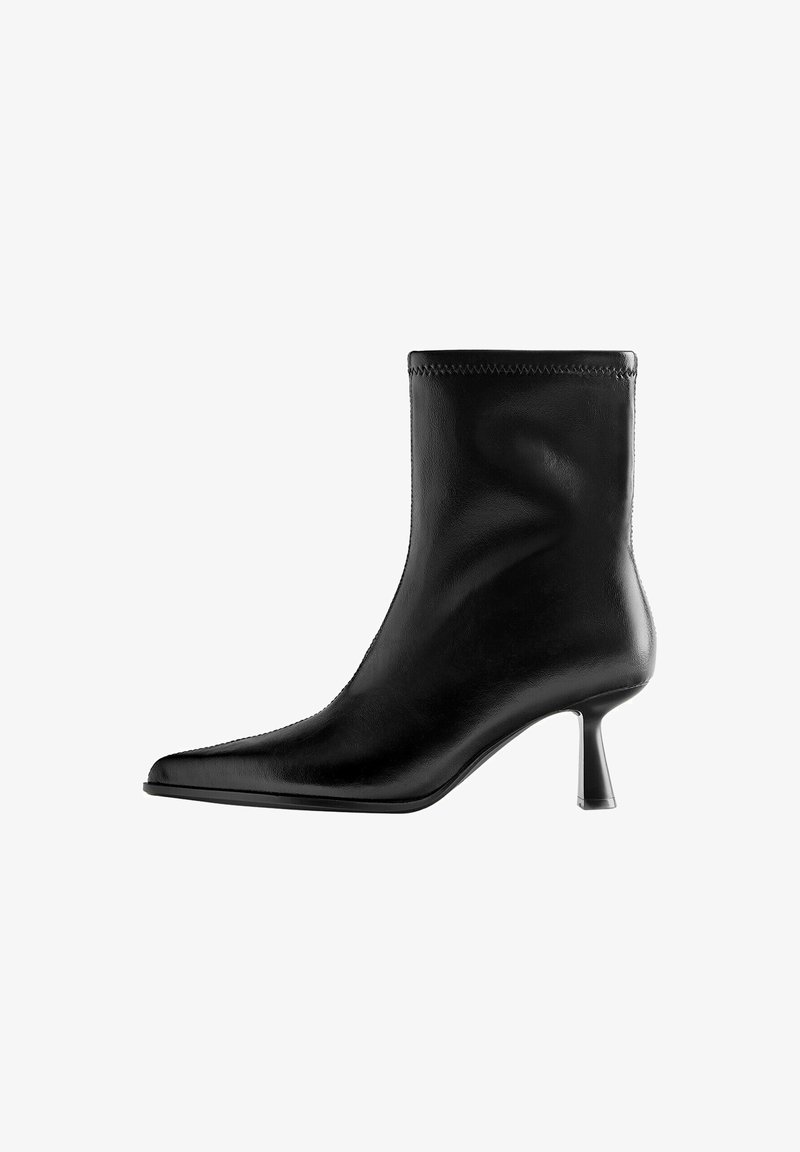 Bottine en cuir noir avec bout pointu et talon moyen et fin sur fond blanc.