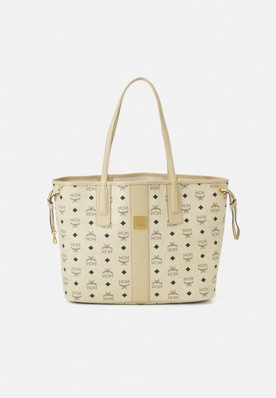 Sac fourre-tout beige en matériau synthétique, avec un motif de logo répété, deux poignées et une finition en métal doré.