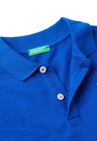 Polo blu realizzato in tessuto testurizzato con colletto classico. Presenta due bottoni bianchi e un'etichetta verde con la scritta "UNIFIED COLORS OF BENETTON."