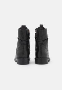 Botas de cuero negras hasta el tobillo con una textura suave, puntera redondeada y tacón apilado. Presentan cierre de cremallera y un lazo decorativo en la parte posterior.