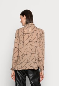 Beige Bluse mit schwarzem geometrischem Linienmuster, langen Ärmeln, einem Rüschenausschnitt und einem Schlüssellochverschluss auf der Rückseite. Glatte Stoffstruktur.