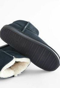 Navy blue suede slippers with a soft cream lining, featuring a textured black rubber sole and contrasting stitching along the seams.