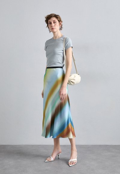 Gray fitted t-shirt paired with a flowy, multicolored skirt featuring wavy blue, brown, and cream patterns. White heels and a small beige bag.
