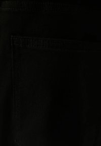 Tissu noir à texture lisse, avec une seule poche cousue. Le design général est simple et sans ornements.