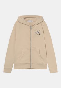 Sudadera con cremallera en color beige, con un bolsillo tipo canguro, puños y dobladillo de canalé. Presenta un logo en el lado izquierdo del pecho en gris. Fabricada con tejido suave.