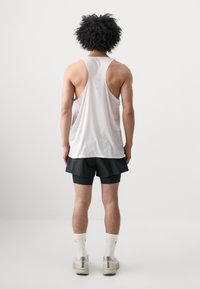 White sleeveless tank top with a textured pattern, paired with black shorts. The person is wearing white socks and light-colored sneakers.
