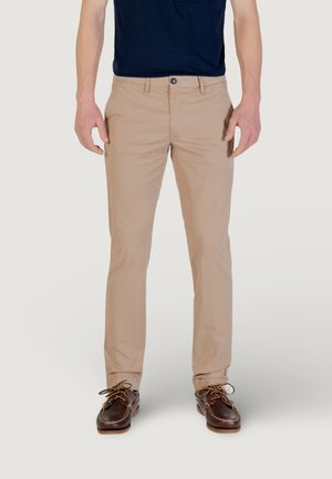 Chinos en coton marron clair avec une coupe slim, dotés d'une fermeture à un bouton et de poches avant. Portés avec des chaussures bateau marron foncé.