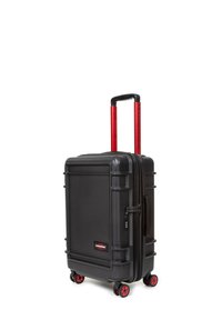 Black hardshell suitcase with four red wheels, retractable red handle, textured surface, branded accents, and combination lock on the side.