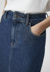 Jupe en denim bleu foncé à taille haute, dotée d'une fermeture à boutons, de coutures visibles et de deux poches latérales. Texture lisse.
