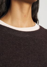 Dunkelgrauer Wollpullover mit Rundhalsausschnitt, der über einen kontrastierenden, hellen gerippten Kragen und eine weiche, strukturierte Oberfläche verfügt.