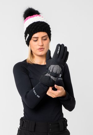 Black outdoor gloves with gray accents, adjustable strap, and textured grip. Model wears a black long-sleeve top and a multi-colored beanie.