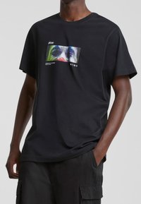 Czarny bawełniany t-shirt z kolorowym nadrukiem graficznym z przodu, przedstawiającym abstrakcyjne rysy twarzy oraz biały tekst. Krótkie rękawy, luźny krój.