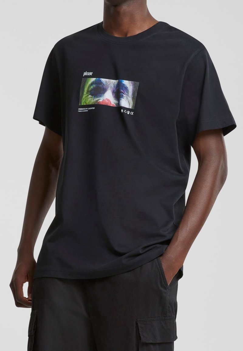 Czarny bawełniany t-shirt z kolorowym nadrukiem graficznym z przodu, przedstawiającym abstrakcyjne rysy twarzy oraz biały tekst. Krótkie rękawy, luźny krój.