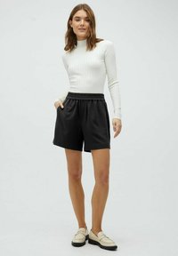 Zwarte, losse shorts van zachte stof met een elastische tailleband. Gecombineerd met een geribde, witte top met lange mouwen en lichte schoenen.