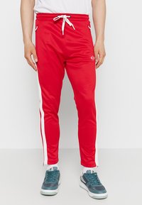 Rode sportbroek met een taps toelopende pasvorm, witte zijkanten, elastische tailleband, trekkoordsluiting en logo-detail op bovenbeen.