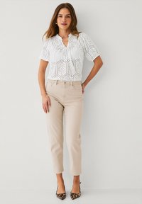Hvid blondebluse med korte ærmer, med en rund halsudskæring; parret med beige tapered bukser og leopardmønstrede hæle.