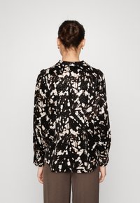Blusa astratta nera e crema con finitura texturizzata, maniche lunghe e collo rotondo, caratterizzata da una vestibilità morbida.