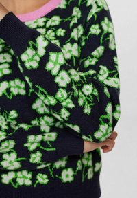 Sweter dziany z granatowym tłem ozdobiony jasnymi zielonymi i białymi kwiatowymi wzorami. ściągacze na rękawach i różowy okrągły dekolt.