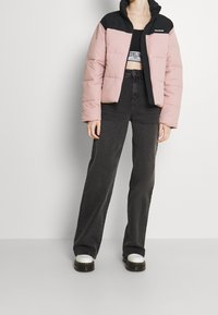 Pink and black puffer jacket with a cropped design, featuring a zip front and quilted texture. Paired with high-waisted black jeans and white shoes.