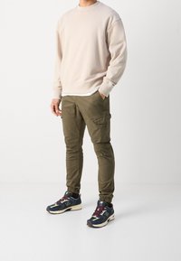 Beige sweatshirt met ronde hals, olijfgroene cargobroek en marineblauwe sneakers met bordeaux accenten; aansluitend ontwerp met elastische boorden en zakken.