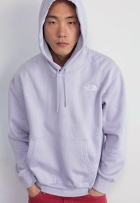 Felpa di cotone lavanda con tasca frontale e cordini. Presenta un piccolo logo bianco sul lato sinistro del petto e orlo a coste.