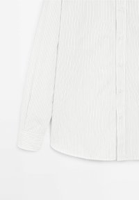 Chemise blanche à manches longues à rayures fines noires verticales, boutonnée sur le devant et manches avec poignets. Texture lisse, forme classique.