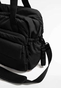 Borsa nera imbottita con numerosi scomparti con zip, superficie testurizzata, manici in tessuto resistenti e una tracolla regolabile.