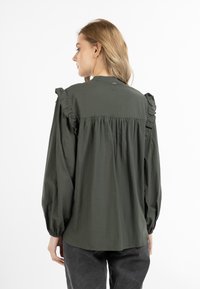 Olijfgroene blouse met rimpelige schouderaccenten, lange ballonmouwen en een relaxte pasvorm. Gemaakt van een lichtgewicht stof, met een rugplooi-detail.