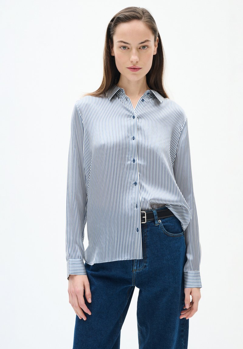 Camicia a righe blu e bianca realizzata in tessuto morbido, con chiusura a bottoni, colletto e maniche lunghe, abbinata a jeans scuri a vita alta.