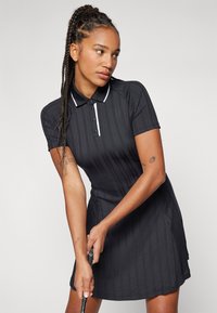 Must mustre golfikleit lühikeste varrukatega, soonikkoes, kraega kaelus, kolm nuppu ja valged aktsendid. Omab sobivat siluetti.