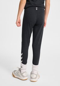 Ciemnoszare legginsy o dopasowanym kroju, z białym wzorem w zygzak po bokach, zestawione z białymi i szarymi butami sportowymi oraz prążkowanymi skarpetkami.
