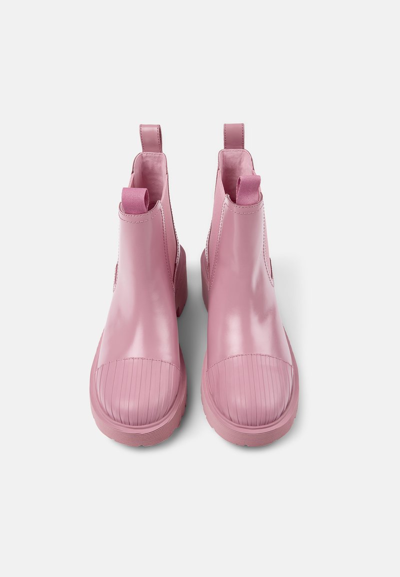 Bottines roses en matériau brillant, avec des embouts côtelés, des tirettes et des panneaux latéraux élastiques pour un enfilage facile.