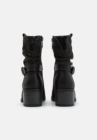 Botines negros hasta el tobillo con un diseño arrugado, que presentan un cierre lateral, un cinturón decorativo con patrones recortados y un tacón apilado.