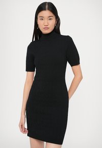 Crna pletena haljina s visokim ovratnikom i kratkim rukavima, izrađena s teksturiranim uzorkom i uskim krojem koji završava iznad koljena.