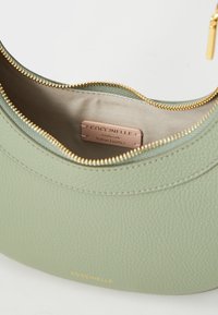 Light green leather bag with a smooth texture, rounded shape, gold zipper, and beige lining featuring a label that reads "Coccinelle Authentic Italian Leather."