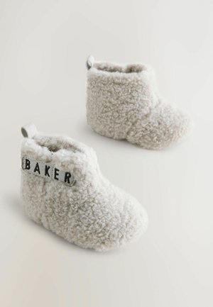 Behagelige beige futter med blød tekstur og rund form. Har et gråt mærke med teksten "BAKER" på ydersiden samt en bagestrop for nem påtagning.