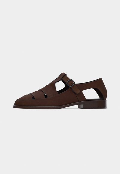 Brun lädersandal för män med stängd tå, utskurna sidor, låg klack och justerbar spännbandsrem.