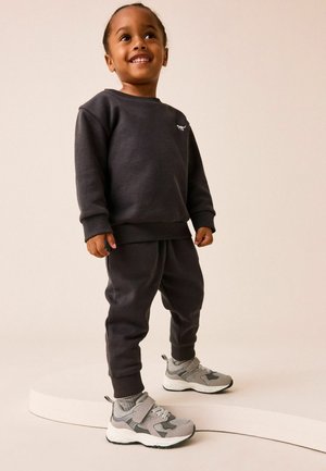 Sweatshirt gris et joggers assortis en tissu doux ; dotés de poignets côtelés et d'un petit logo. Baskets grises avec des accents en maille et une sangle.
