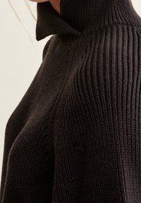 Svart ribbad stickad tröja med hög krage och textilstruktur. Sidoprofilen visar struktur och design utan dekorationer.