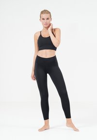 Zwarte sportbeha met dunne bandjes, gecombineerd met hoge zwarte leggings. Beide hebben een gladde, rekbare stof. Geen zichtbare patronen.