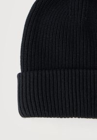 Μαύρο πλεκτό σκουφάκι με κάθετες ραβδώσεις και διπλωμένο γείσο, σε απλό φωτεινό φόντο.