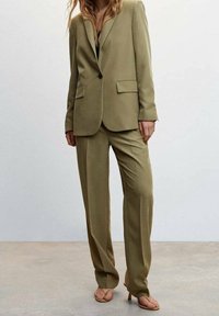 Completo su misura verde oliva con blazer a un bottone, rever a punta e due tasche frontali; abbinato a pantaloni dritti e sandali color nude.
