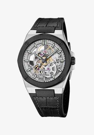 Skelettuhr mit sichtbaren Zahnrädern, schwarzer Lünette, silbernem Gehäuse, lumineszierenden Stundenmarkierungen und Zeigern sowie schwarzem Lederarmband mit Naht.