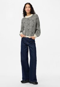 Strickpullover mit einem schwarz-weißen Rautenmuster, kombiniert mit dunkelblauen weiten Jeans. Der Pullover hat einen cremefarbenen Rundhalsausschnitt und Bündchen.