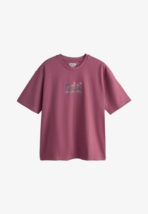 Lila oversized póló, hímzett kék, sárga és lila virágokkal, valamint a mellrészen kurzívával írt „Fleur Après Minuit” szöveggel.